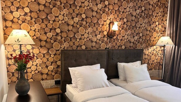 A hotel room with a bed, bedside lamps, a vase with flowers, and a wall covered with logs. - Hnameni Stepanavan Guesthouse (Step'anavan)