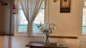 A room with a wooden table, a vase of white flowers, a fire extinguisher, and a framed picture on the wall. - Hnameni Stepanavan Guesthouse (Step'anavan)