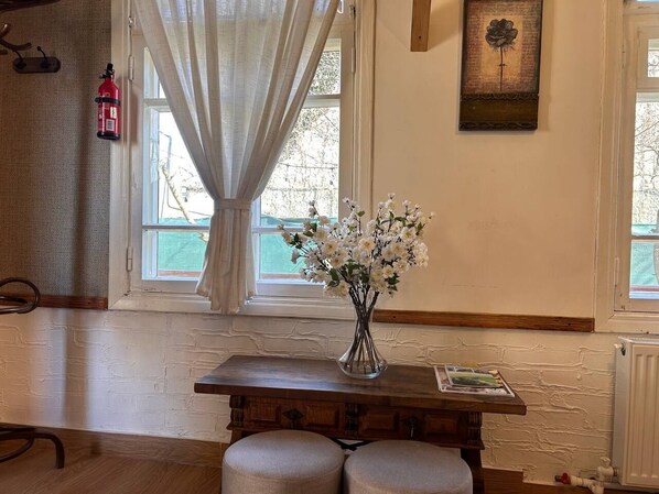 Une pièce avec une table en bois, un vase de fleurs blanches, un extincteur et un tableau encadré accroché au mur.