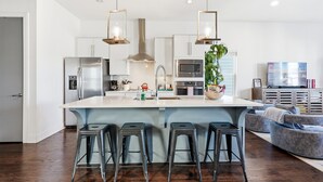 Une cuisine moderne dotée d’un îlot central, d’appareils électroménagers en acier inoxydable et de tabourets de bar.