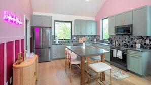 Una cocina moderna con armarios grises, un refrigerador de acero inoxidable, un salpicadero con estampado blanco y negro y un letrero de neón en la pared.