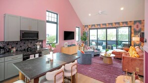 Una cocina moderna con armarios grises, un microondas negro y una zona de comedor con una mesa oscura y sillas rosas.