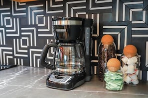 Una cafetera sobre una encimera con dos tarros de vidrio que contienen granos de café y cápsulas.