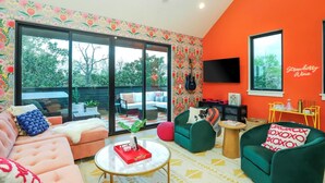Ein modernes Wohnzimmer mit einem großen Schiebeglasfenster zum Außenbereich, einem Deckenventilator und einem Flachbildfernseher an der orangefarbenen Wand.
