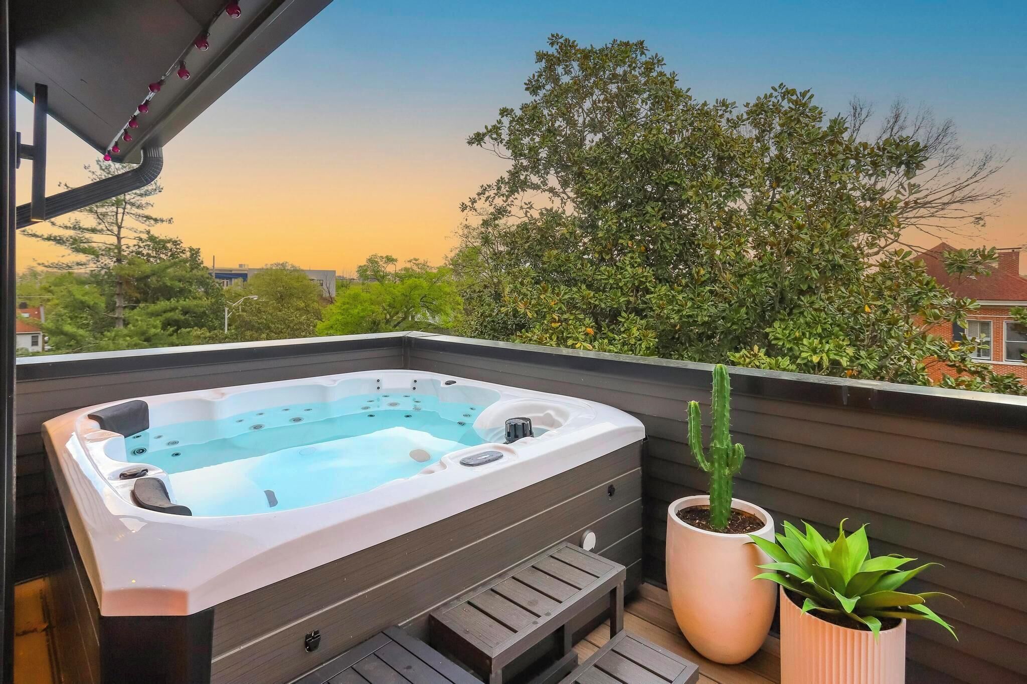 A hot tub on a wooden deck with a view of trees and houses.