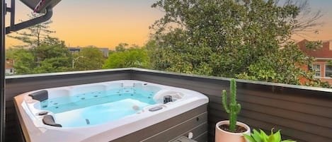 A hot tub on a wooden deck with a view of trees and houses.