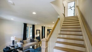 A spacious living room with a staircase, a sofa, a coffee table, and a lamp. - Belmont Luxe | Walk to Hillsboro, Belmont & 12 So (Nashville)