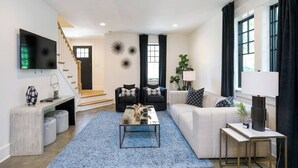 A modern living room with a staircase, a flat-screen TV, and a coffee table. - Belmont Luxe | Walk to Hillsboro, Belmont & 12 So (Nashville)