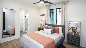 A bedroom with a bed, bedside lamps, a ceiling fan, a large window with curtains, and a mirror on the wall. - Belmont Luxe | Walk to Hillsboro, Belmont & 12 So (Nashville)