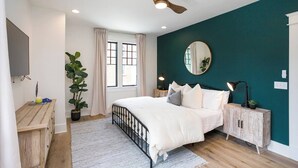 A bedroom with a bed, bedside tables, a mirror, a ceiling fan, and a window with curtains. - Chic Belmont Retreat | Walk to Hillsboro & 12 South (Nashville)