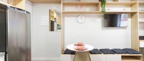 A modern kitchen with a built-in refrigerator, a dining area with a round table, and a flat-screen TV mounted on the wall.