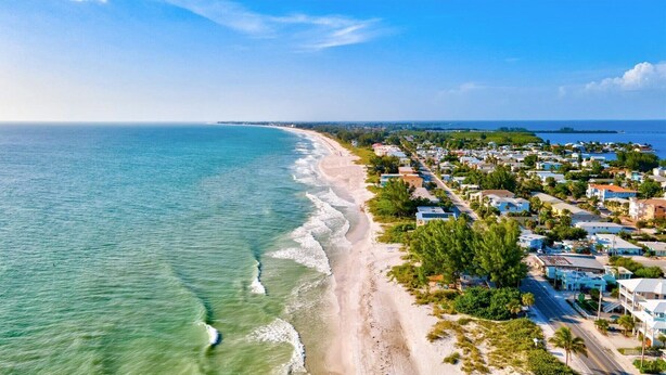 Zona residencial costera con casas a lo largo de la playa, cielo despejado y el océano.