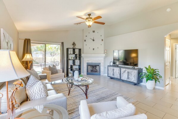 Relax in this spacious living room with a sofa set, coffee table, and TV on a cabinet, plus a ceiling fan and a fireplace.