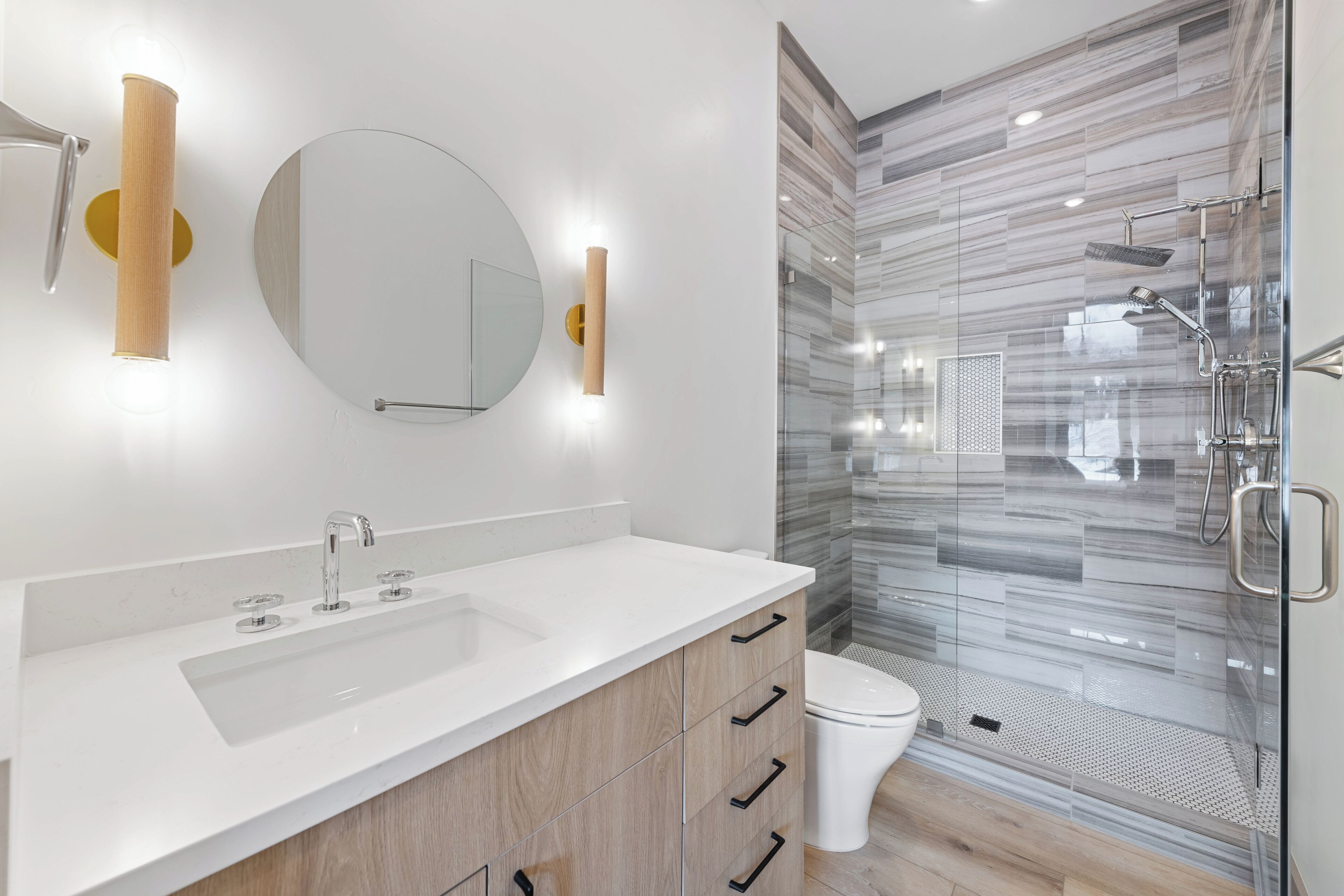 A modern bathroom with a white sink, wooden cabinets, a large mirror, and a glass-enclosed shower area.