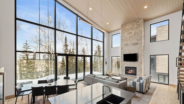 A modern kitchen with a large island, a dining area with a view of trees, and a fireplace. - Modern Ski-in/out Home in Brian Head w/ Deck (Brian Head)