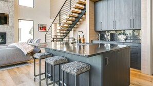 A modern kitchen with a central island, bar stools, and a staircase. - Modern Ski-in/out Home in Brian Head w/ Deck (Brian Head)