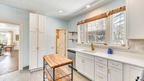 Una cocina moderna con armarios blancos, una mesa de madera y una ventana con persiana de bambú.