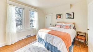 Un dormitorio con una cama grande, una ventana con cortinas, una puerta y dos cuadros en la pared.