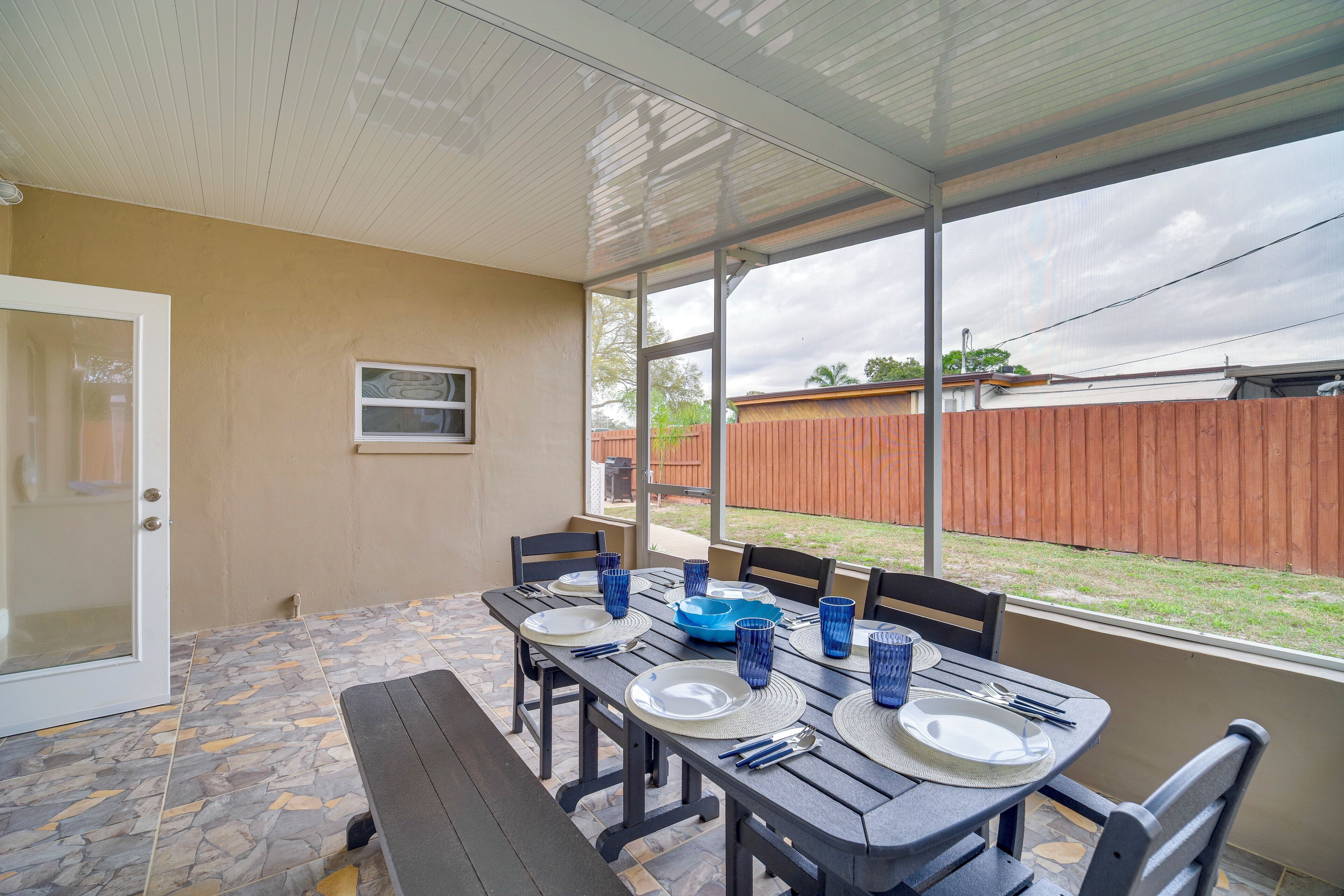 Eine überdachte Terrasse mit Tisch für vier Personen, Steinboden und Blick auf einen Garten.