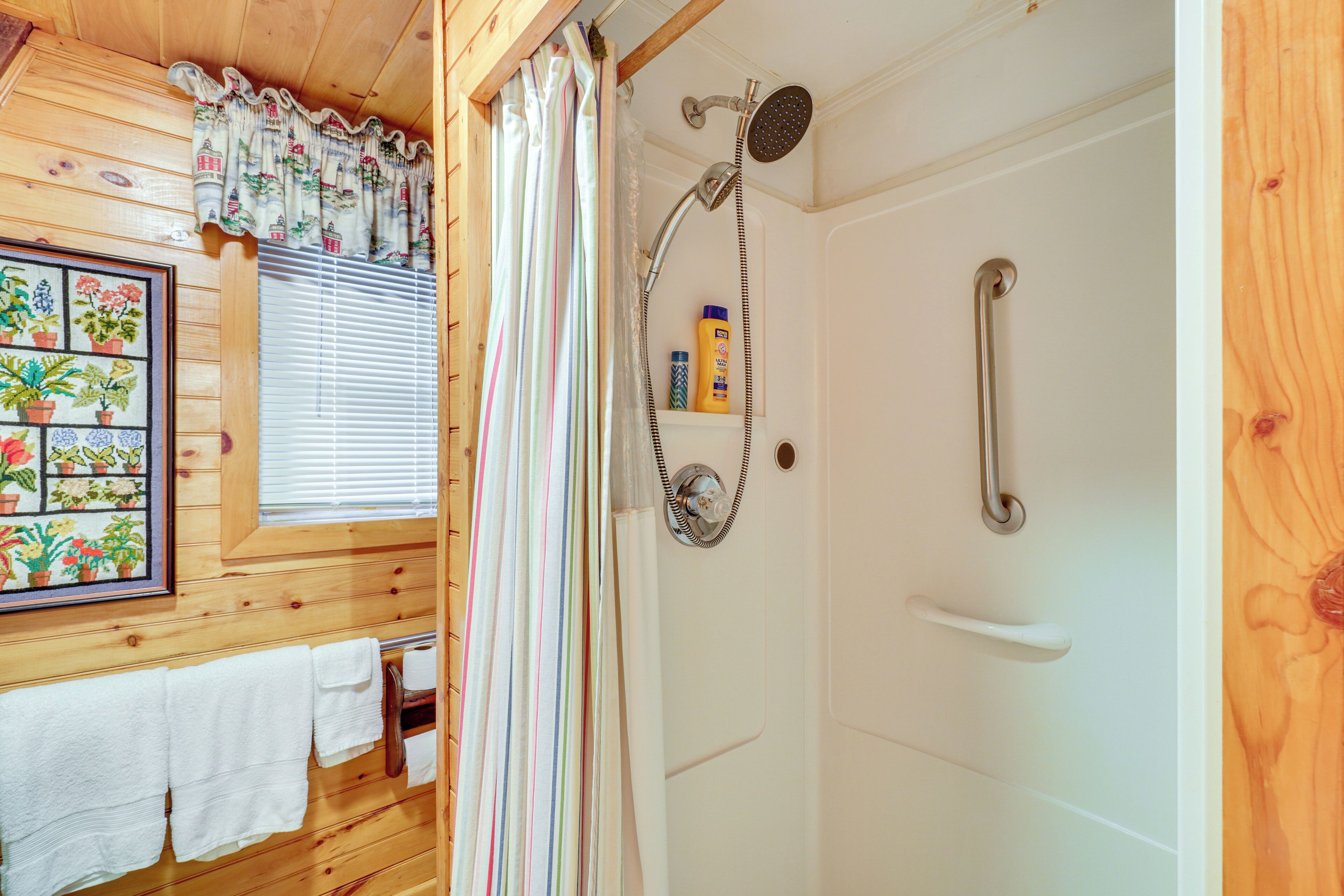 A wooden cabin bathroom with a shower, a window with blinds, and a framed botanical print on the wall.