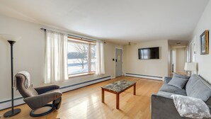 A living room with a sofa, a massage chair, a coffee table, and a TV mounted on the wall. - Deck & Fire Pit: Cozy Escape in Morrisville! (Morrisville)