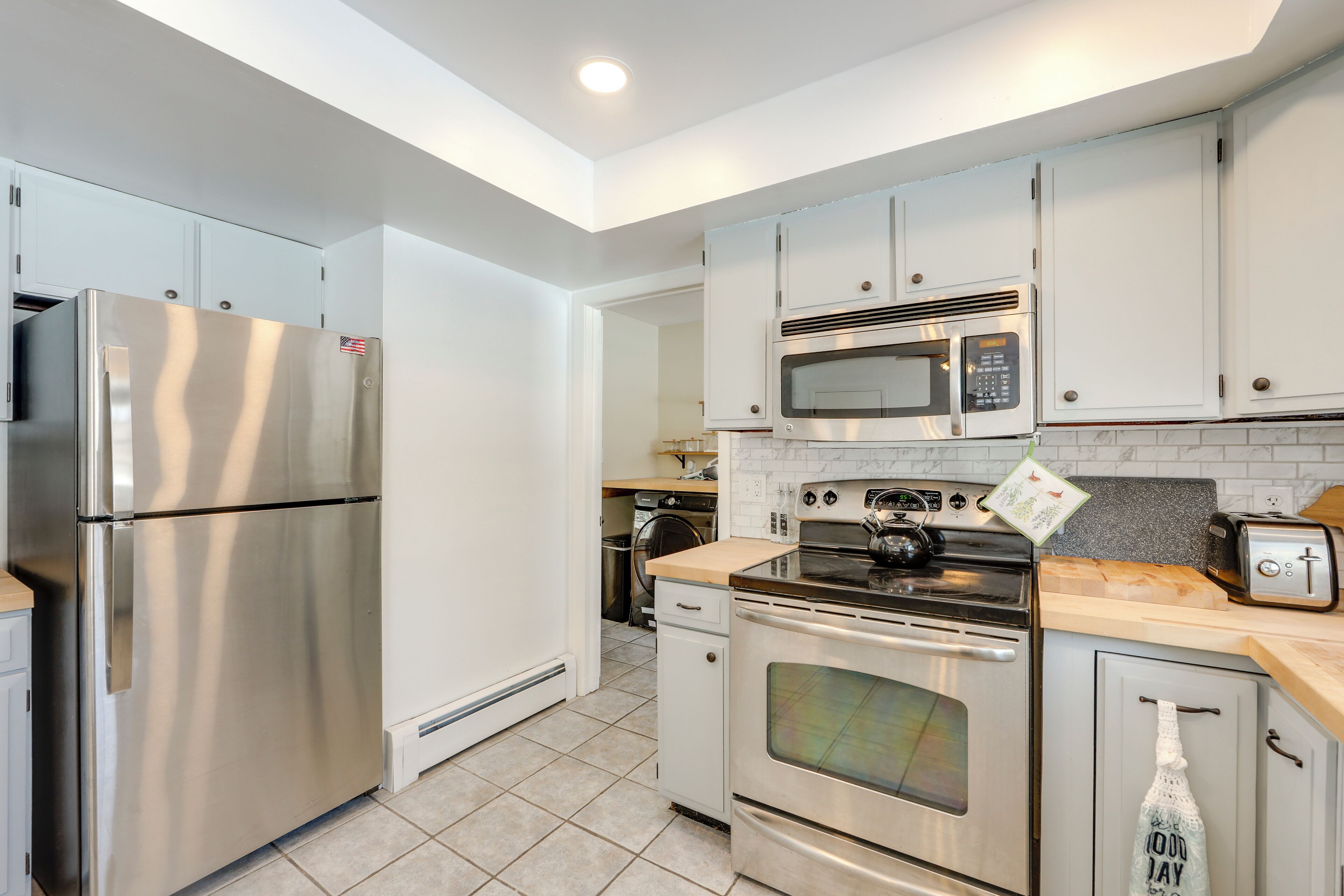A modern kitchen with stainless steel appliances, white cabinetry, and a tiled backsplash.