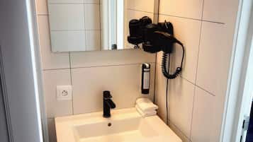 Un bagno con un lavandino bianco, uno specchio e un asciugacapelli fissato alla parete.