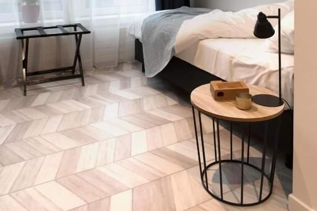 A small, modern bedroom with a bed, a bedside table, a round table, and a potted plant.