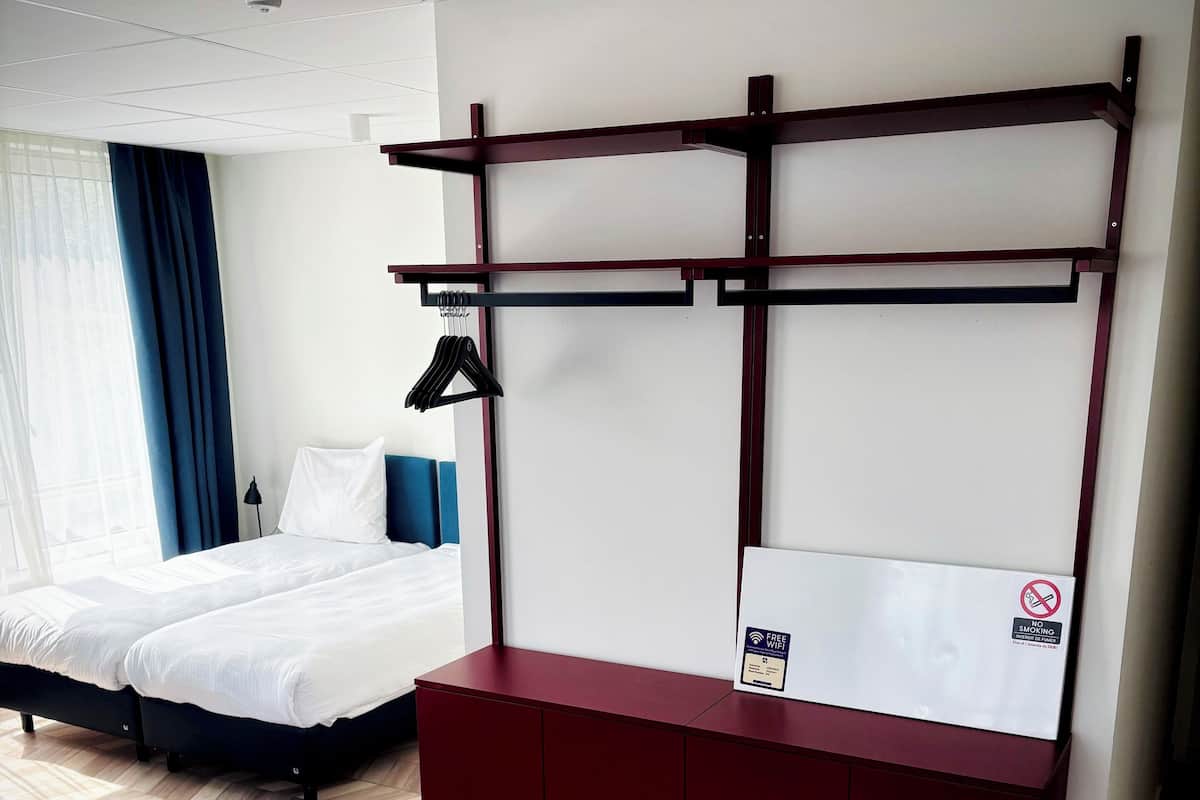 A hotel room with a bed, a desk with a no-smoking sign, and a hanging clothes rack.