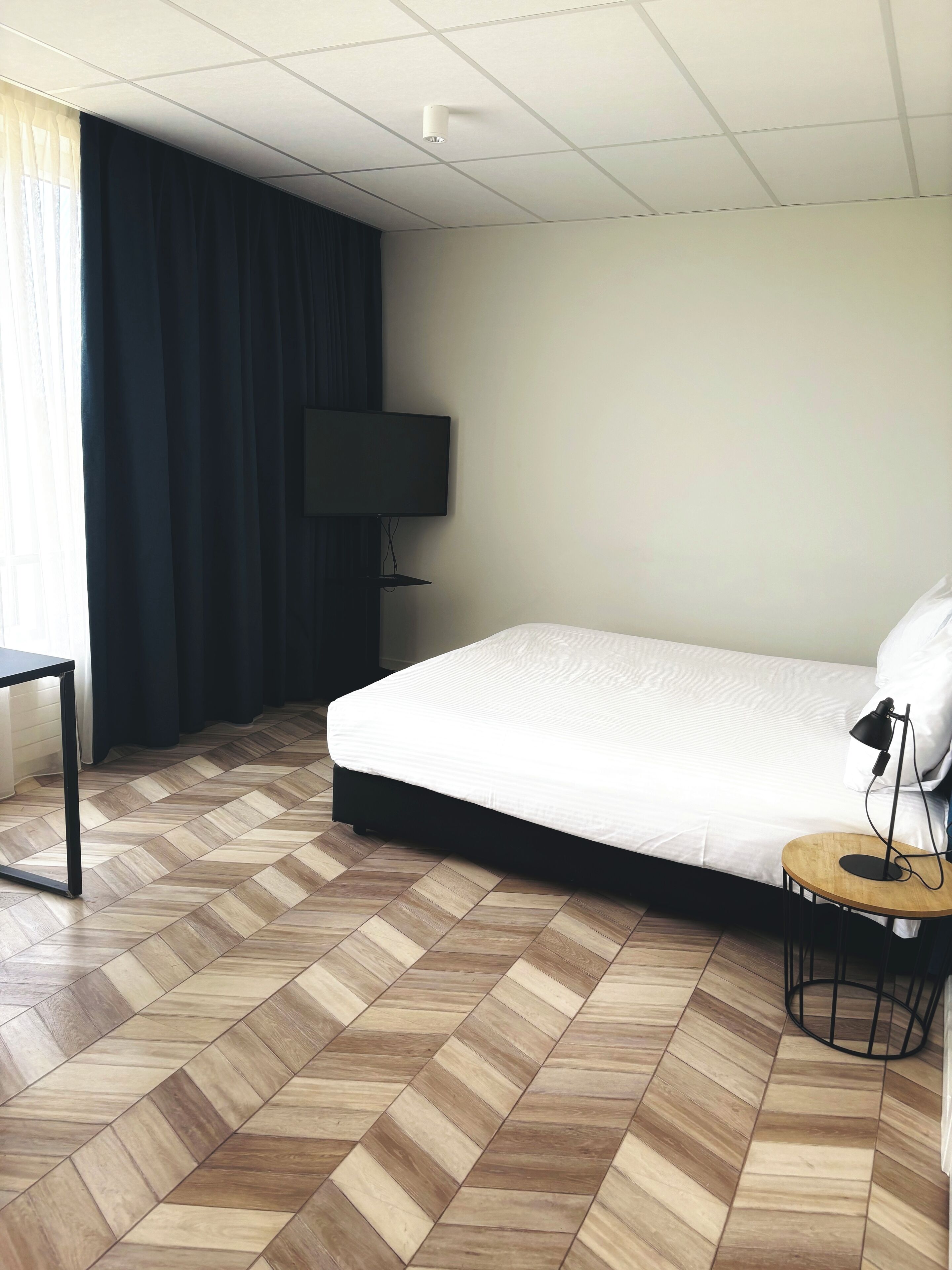 Een hotelkamer met een bed, een bureau, een televisie en een lamp.
