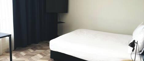 A hotel room with a bed, a desk, a TV, and a lamp.