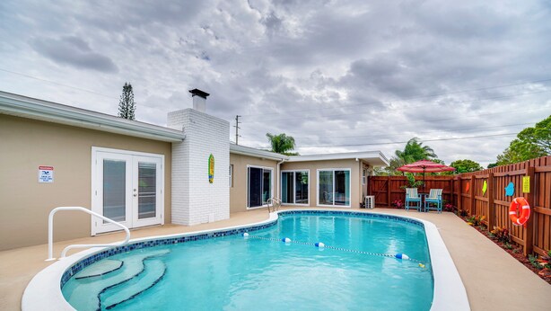 A swimming pool with a white deck, a wooden fence, and a covered patio area with chairs. - 5 Mi to Beaches: Melbourne Duplex w/ Heated Pool! (Melbourne)