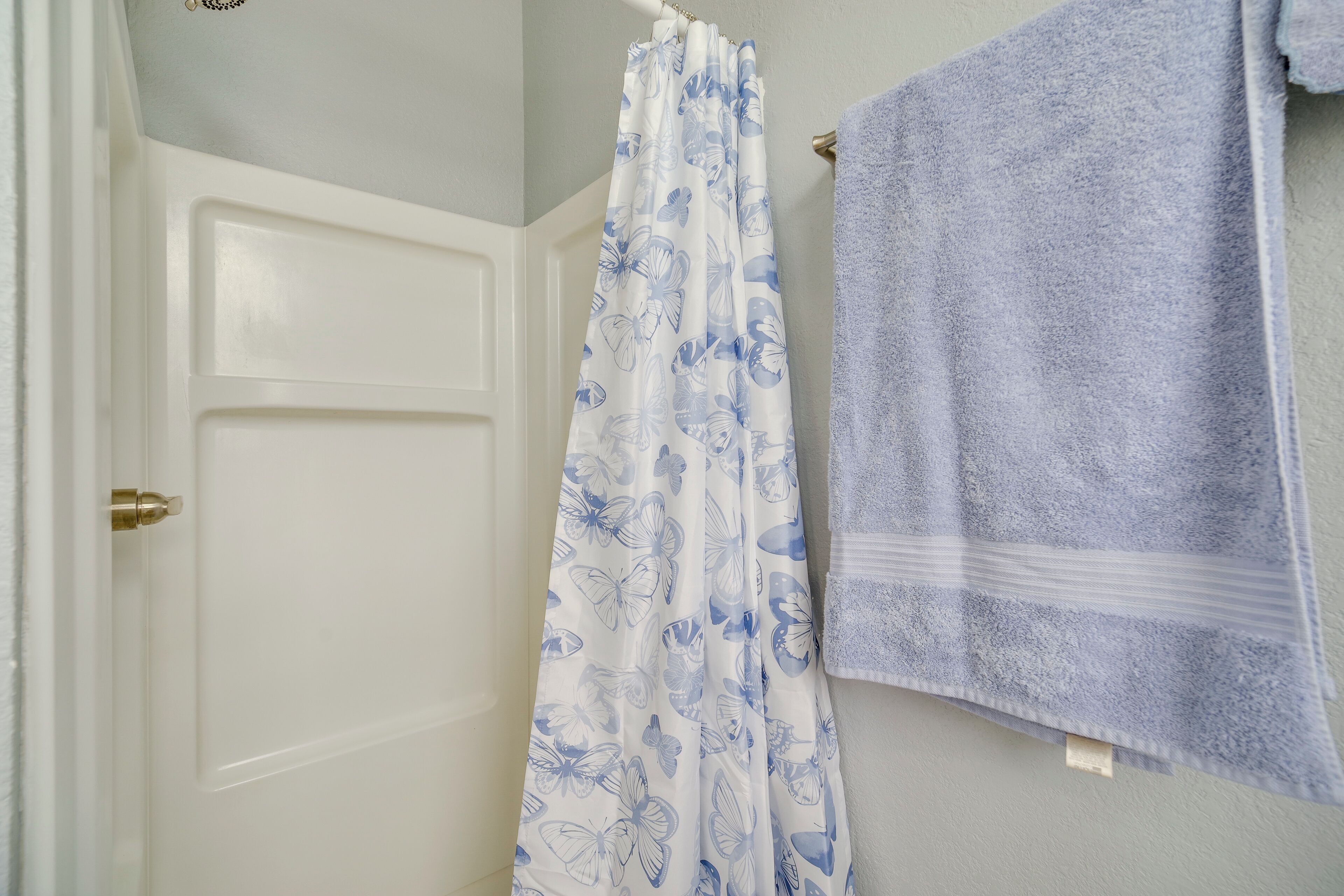 A bathroom with a white door, a shower curtain with a butterfly pattern, and a blue towel hanging on the wall.