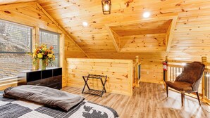 Acogedora habitación tipo cabaña de madera con cama, silla, una mesita y ventana con un arreglo floral.