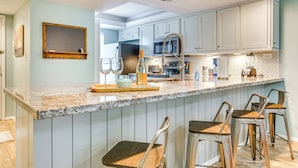 A kitchen with white cabinets, a granite countertop, and bar stools. - Walk to Beach! Condo w/ Pool Access in Texas (South Padre Island)