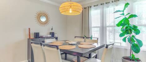 A dining area with a dark wooden table, beige chairs, and a large potted plant.
