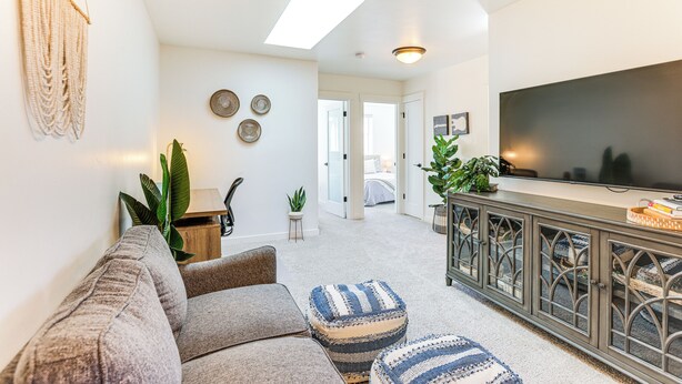 A living room with a sofa, ottomans, a TV, and a staircase leading to another room. - Hike, Bike & Ski: All-season Bend Escape (Bend)