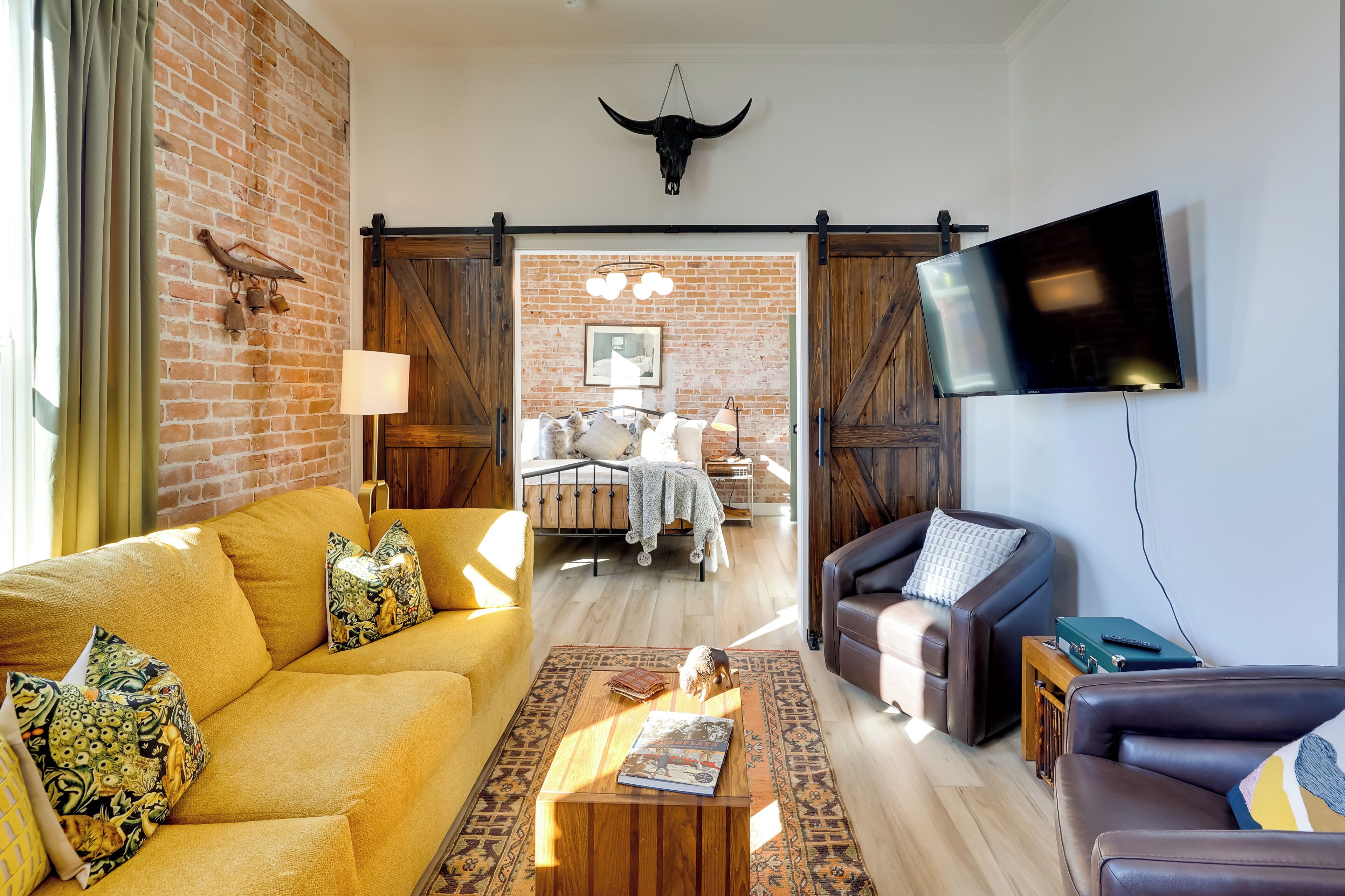 A living room with a yellow sofa, a brown leather couch, a wooden coffee table, and a TV mounted on the wall. - Walk to Shops & Eats: Charming Dtwn Emmett Apt! (Emmett)