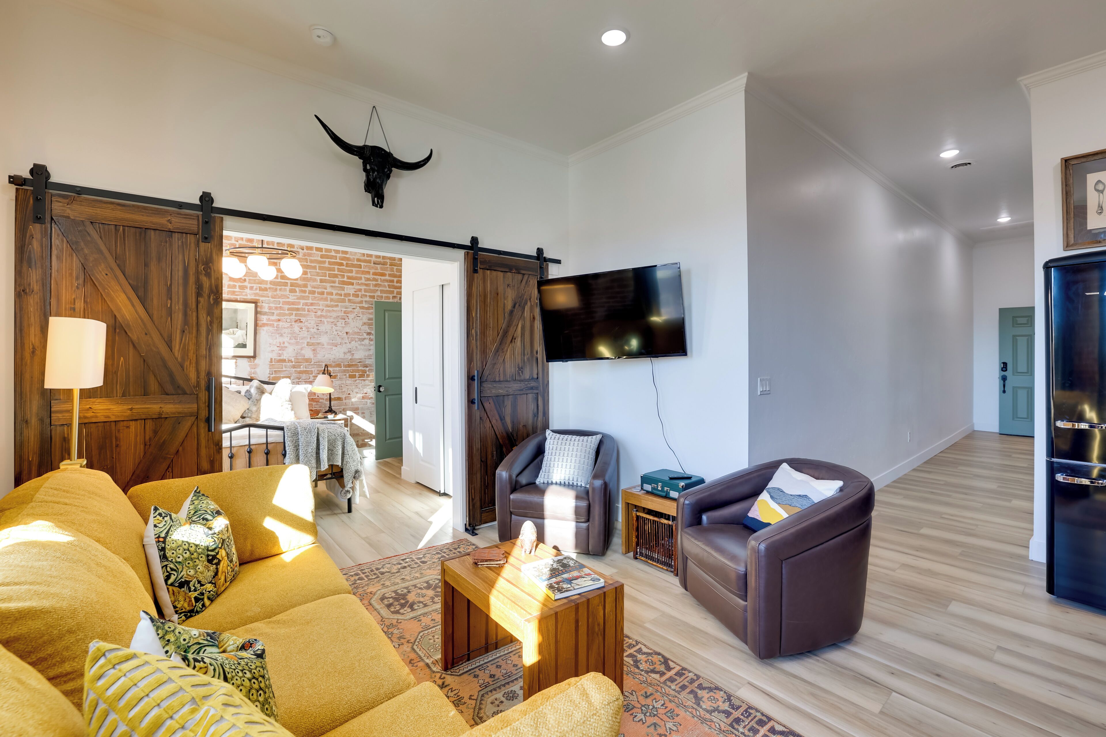 A spacious living room with a sofa, armchairs, a coffee table, and a TV mounted on the wall.