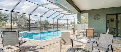 A covered outdoor area with a pool, lounge chairs, and a table.