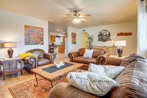 A living room with leather sofas, a coffee table, and a ceiling fan. There is a kitchen in the background. - Patio & Mtn Views: Wickenburg 'trail Head House' (Wickenburg)