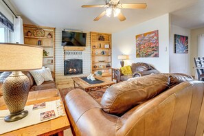 A living room with a fireplace, leather sofa, wooden shelves, and artwork. - Patio & Mtn Views: Wickenburg 'trail Head House' (Wickenburg)