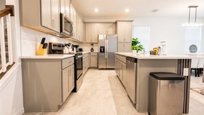 A modern kitchen with stainless steel appliances, a central island, and a trash bin. - Luxury 6BR Pool Home at Solara Resort (Kissimmee)