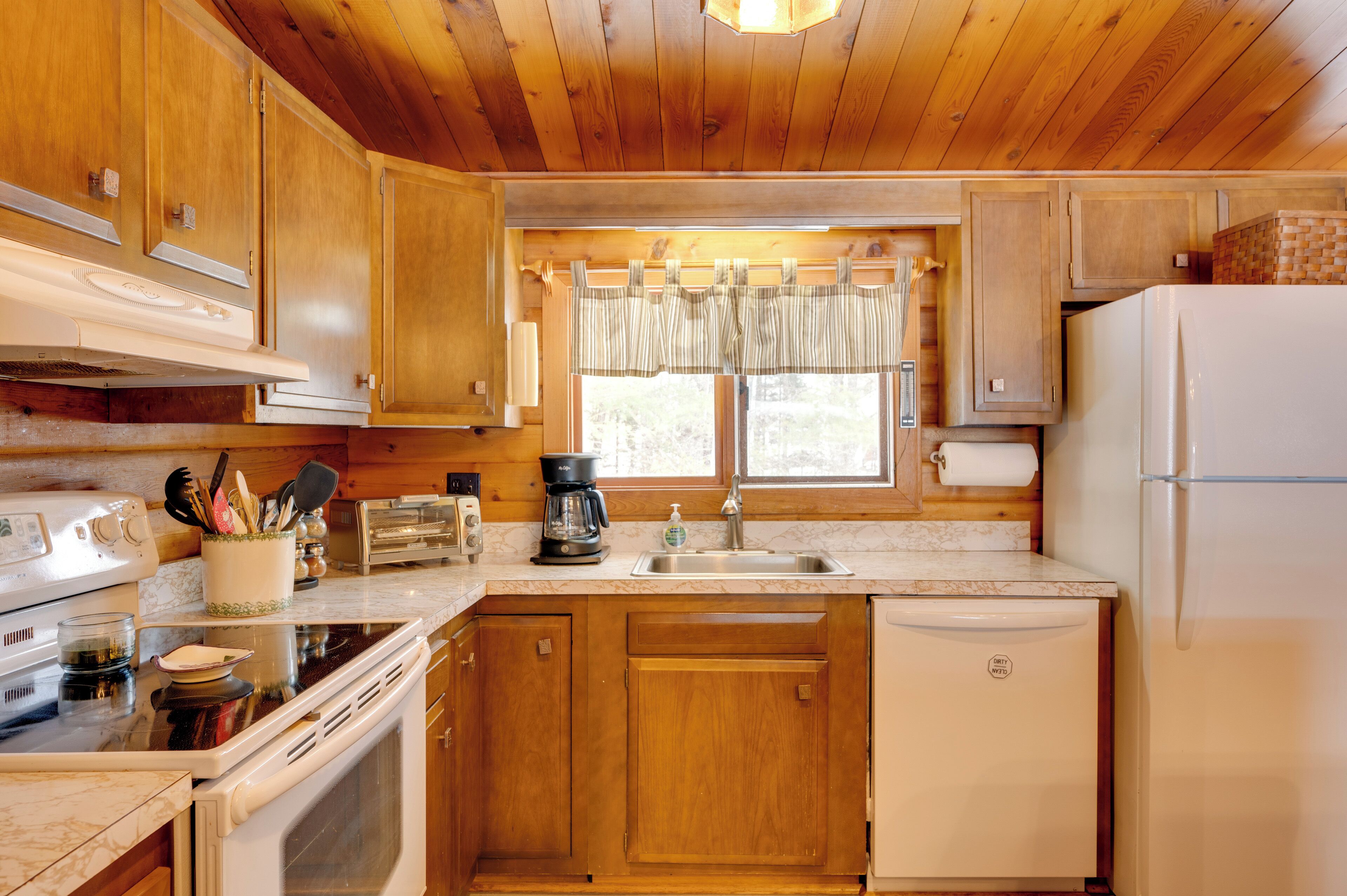 A kitchen with wooden cabinets, a white refrigerator, a stove, a sink, and a window with curtains.