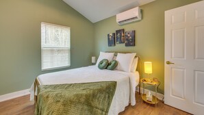 Una camera da letto con un letto, una lampada da comodino, un condizionatore d'aria a parete e un quadro appeso al muro.