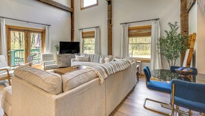 A spacious living room with a large beige sectional sofa, a flat-screen TV, and a dining area with a glass table and blue chairs. - Fish, Hike & Ski: Spacious Family Escape in Eden (Eden)