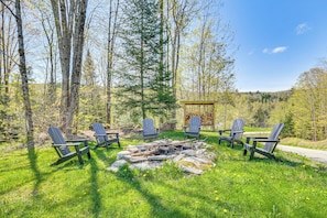 A fire pit with logs surrounded by Adirondack chairs in a forested area. - Fish, Hike & Ski: Spacious Family Escape in Eden (Eden)