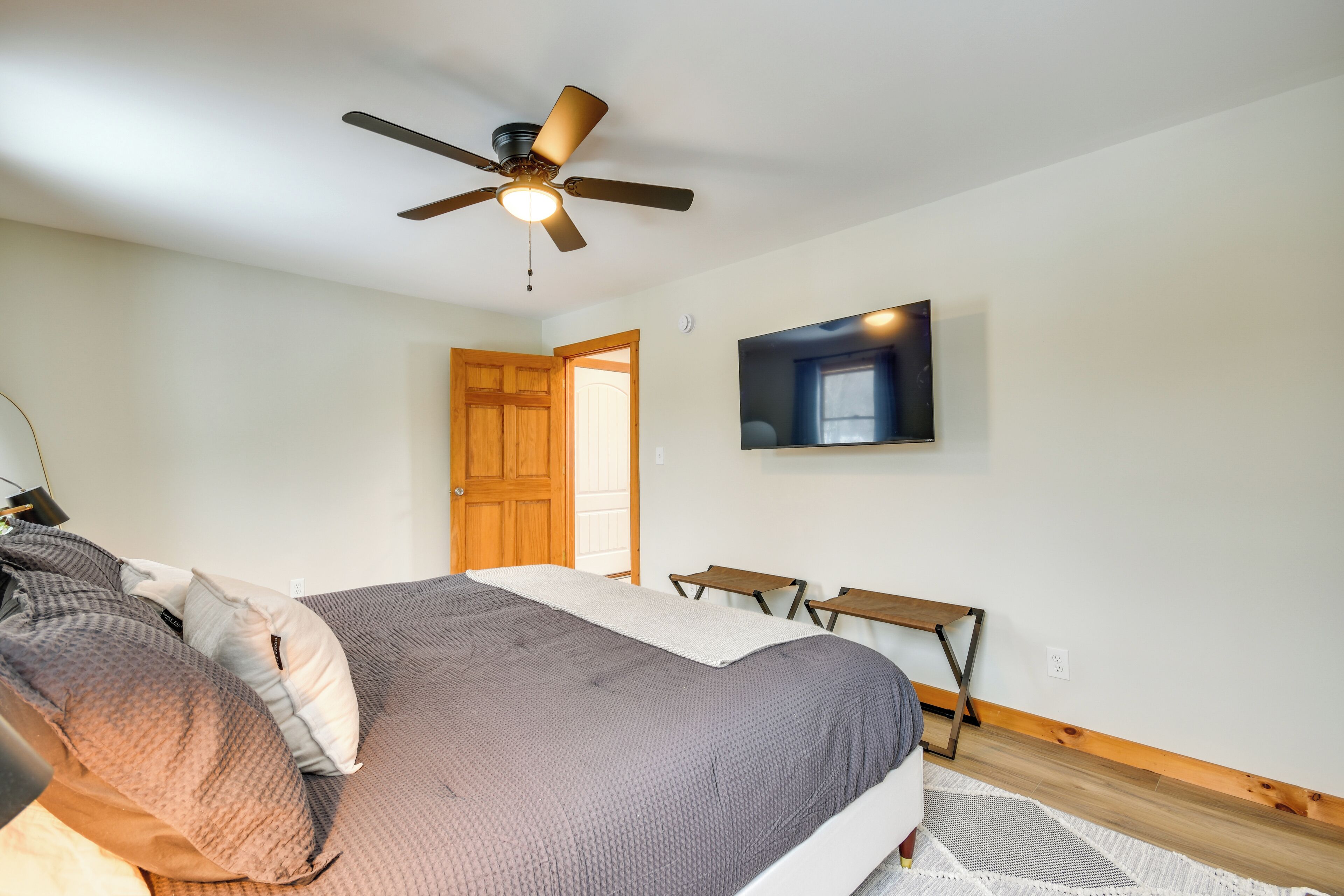 A bedroom with a bed, a ceiling fan, a TV mounted on the wall, and a wooden door.