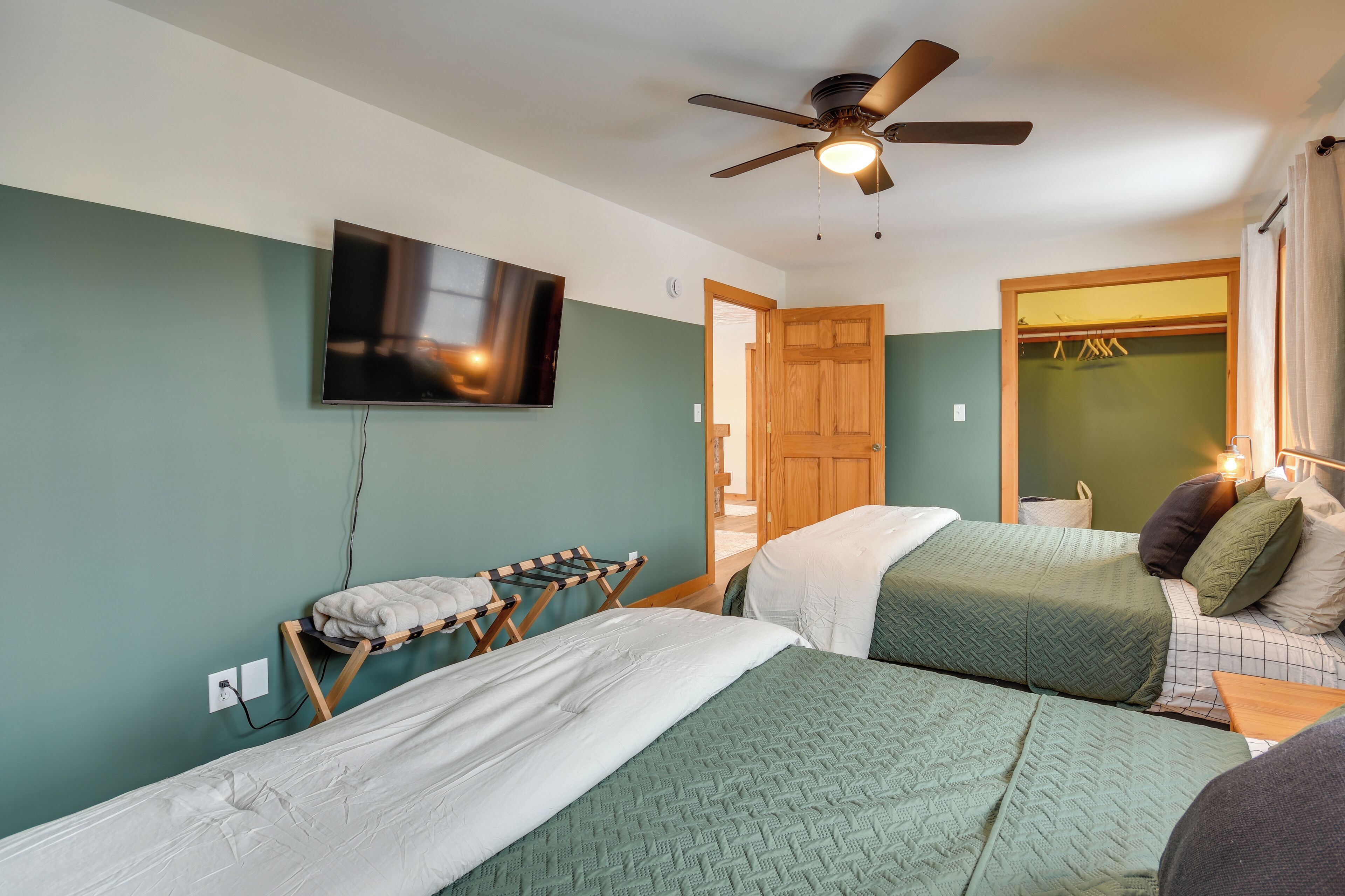 A room with two beds, a ceiling fan, a TV, and a wooden door.