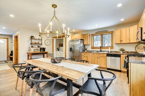 A modern kitchen with wooden cabinets, a stainless steel refrigerator, and a dining area with a wooden table and black chairs.